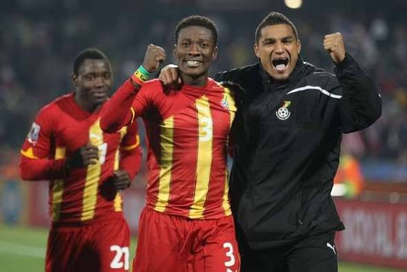 IMG_0629 | Ghanaguardian.com Three football players celebrate on the field, two in red-and-yellow striped jerseys and one in a black jacket, fists raised in joy.