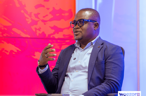 IMG_0644 | Ghanaguardian.com Panelist in a navy blazer and light shirt speaks into a microphone during a studio interview, with a WOEZOR TV logo visible in the corner.
