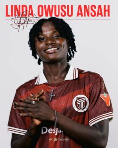 Portrait of Linda Owusu Ansah smiling, wearing a maroon Toronto FC jersey with a cross necklace and hands gently clasped in front.