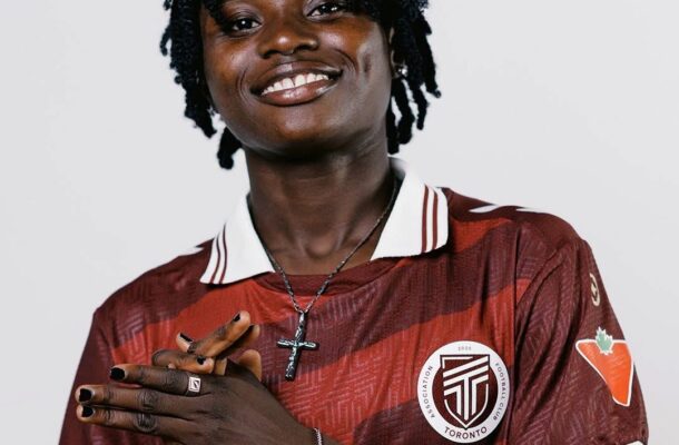Portrait of Linda Owusu Ansah smiling, wearing a maroon Toronto FC jersey with a cross necklace and hands gently clasped in front.