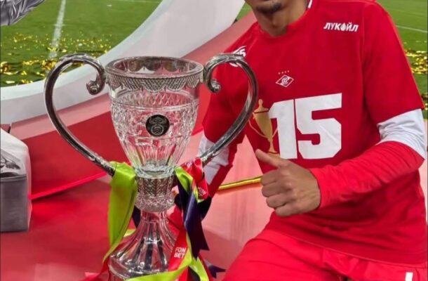 IMG_0670 | Ghanaguardian.com Footballer in red jersey sits beside a large crystal trophy on a red podium, giving a thumbs-up with a stadium background.