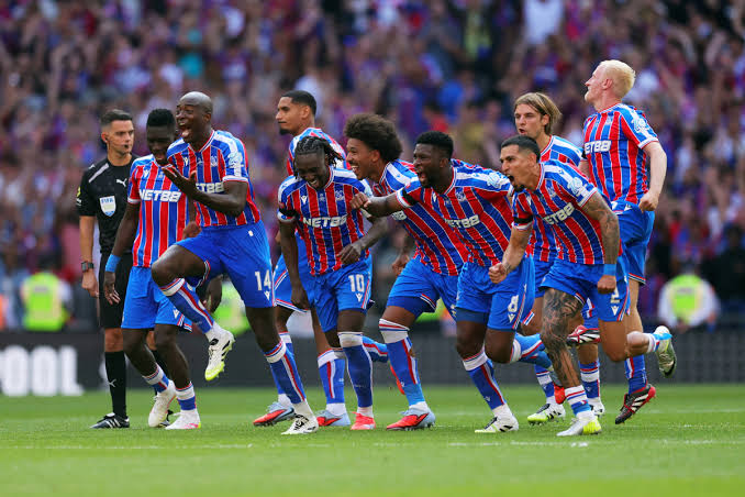 Soccer players in blue and red striped uniforms celebrate a goal, running together on the pitch.