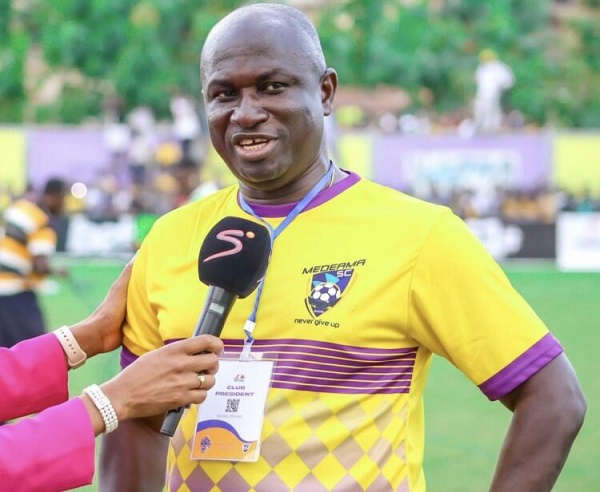 Male football player in a yellow jersey being interviewed on a grassy field, microphone held up to him by a reporter.