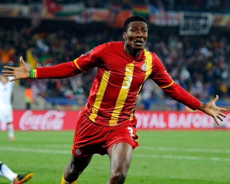 Soccer player in red and yellow stripes celebrating with arms outstretched on the field.