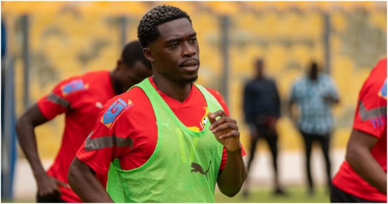 Soccer player in a red jersey and neon green training bib running on a pitch with yellow seats in the background.