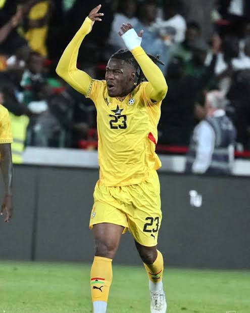 Soccer player in yellow jersey #23 celebrating with arms raised on the field, crowd in background