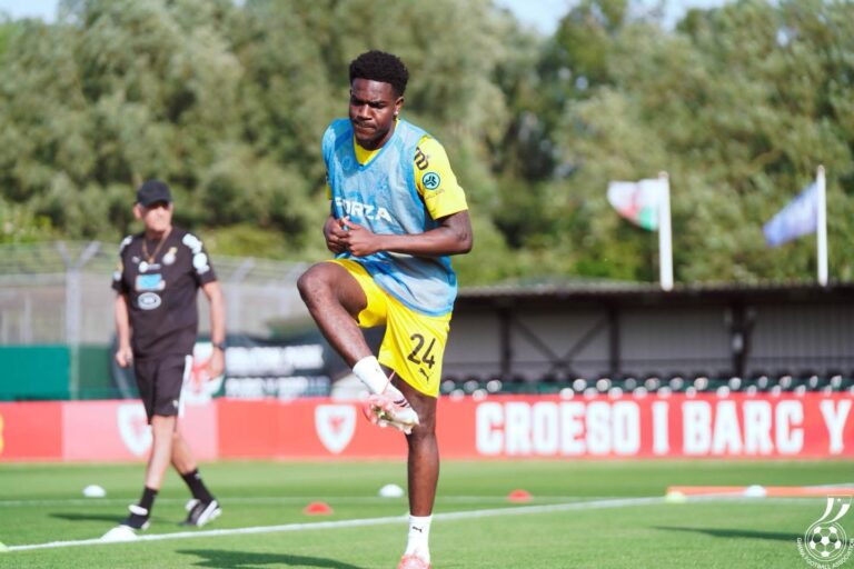 Soccer player wearing yellow shorts and blue training bib mid-air during a drill on a grass field