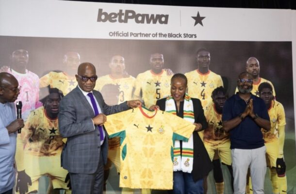 Group of officials presenting a yellow Ghana national team jersey at a BetPawa event, with players on a backdrop that reads 'Official Partner of the Black Stars'.