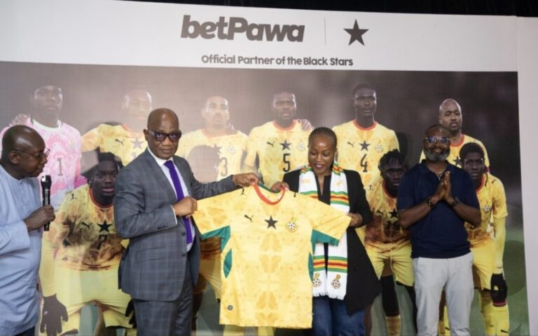 Group of officials presenting a yellow Ghana national team jersey at a BetPawa event, with players on a backdrop that reads 'Official Partner of the Black Stars'.