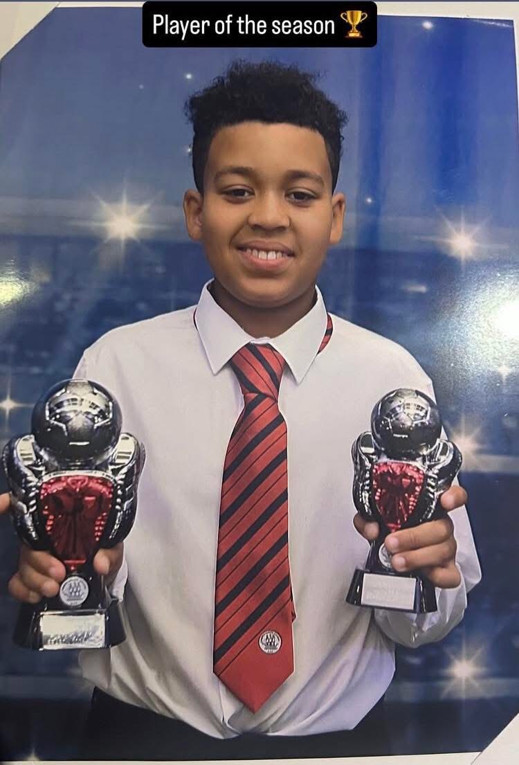 Boy in a white shirt and red striped tie holding two trophies, with a 'Player of the season' banner above—celebrating a sports award.