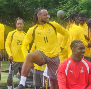 Group of soccer players in yellow training tops outdoors; a man with number 11 lifts his knee while others watch.