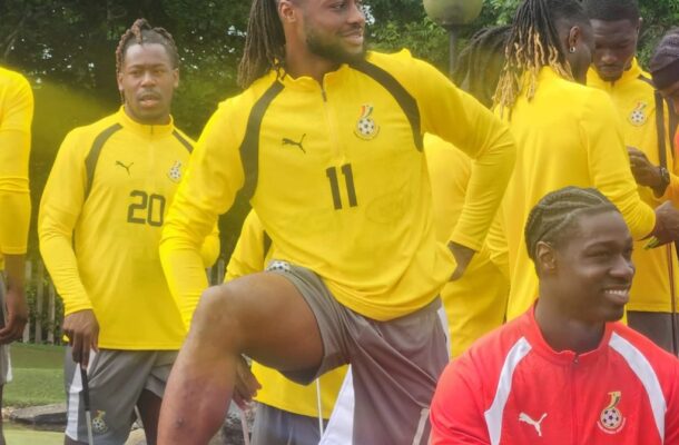 Group of soccer players in yellow training tops outdoors; a man with number 11 lifts his knee while others watch.