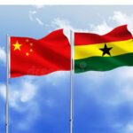 China and Ghana flags fluttering side by side against a clear blue sky with wispy clouds, mounted on flagpoles.