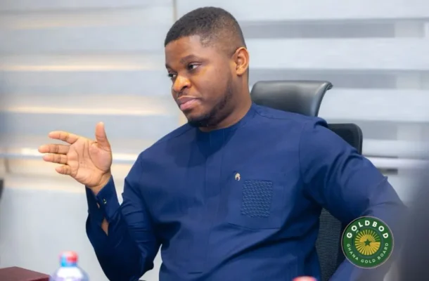 Man in a navy blue traditional shirt sits at a meeting table, gesturing with his left hand as he talks.