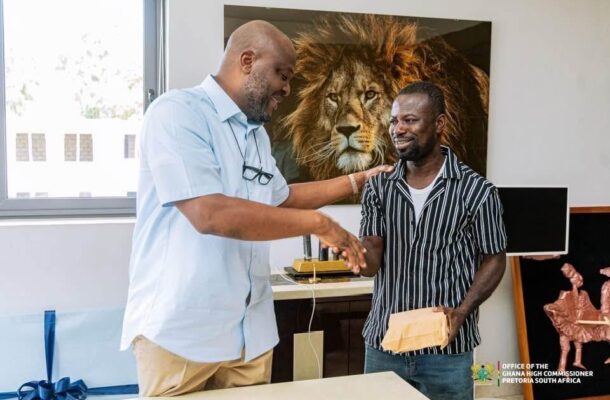 Two men in a bright office shake hands as one passes an envelope to the other, with a large lion portrait on the wall behind them.