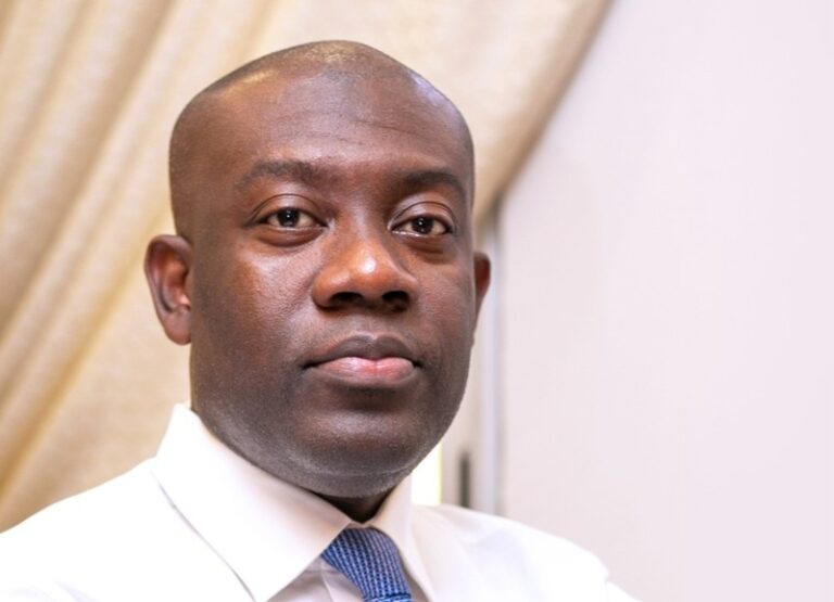 Portrait of a man in a white shirt and blue tie, looking at the camera.