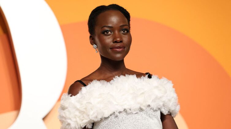 Portrait of a Black woman in a white off-the-shoulder feathered dress, posing against an orange backdrop with soft curved shapes.