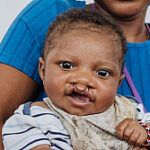 Smiling baby being held by an adult wearing a blue shirt.