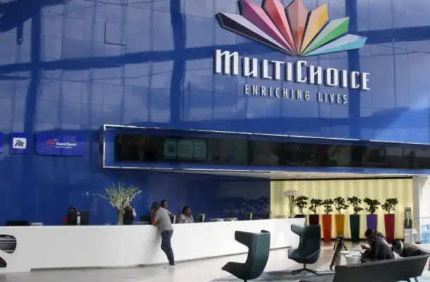 Reception area of a MultiChoice building with a blue exterior and colorful logo, staff behind the counter and visitors seated nearby