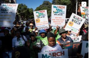 Protesters marching outdoors, holding banners that read 'MARCH AND MARCH UNTIL WE WIN'.