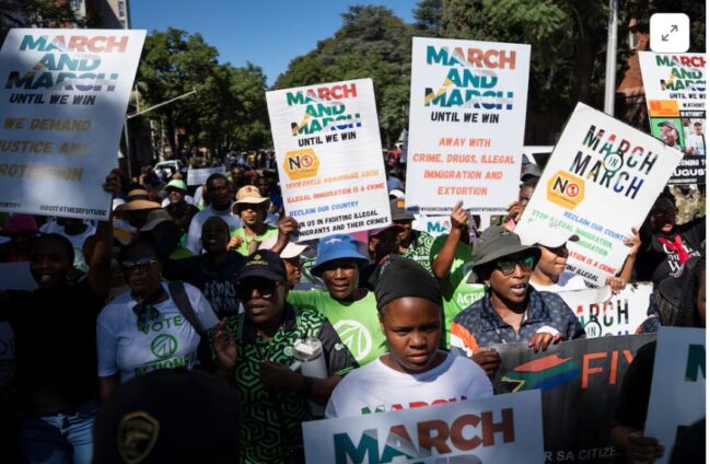 Protesters marching outdoors, holding banners that read 'MARCH AND MARCH UNTIL WE WIN'.