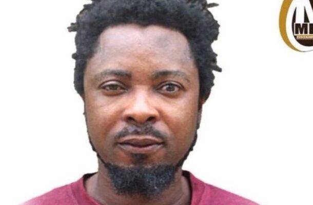 Portrait of Opoku Agyemang with short dreadlocks and a goatee, wearing a red shirt on a white background with a partial circular logo to the right.
