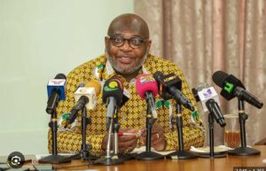 Man in a patterned yellow shirt speaks at a press conference with multiple microphones in front of him.