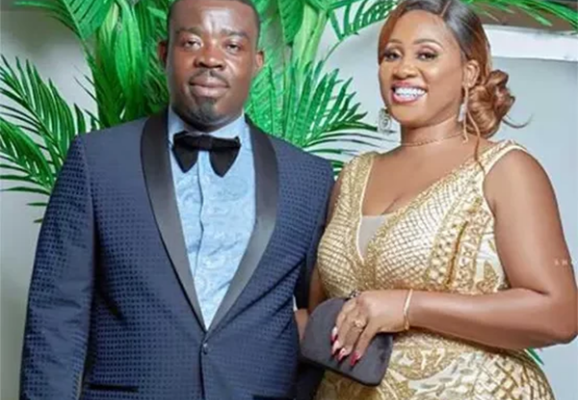 Richard-Nii-Armah-Quaye-and-Joana-Quaye-553x4063-1-578x424 | Ghanaguardian.com Man in a navy tuxedo and bow tie stands beside a woman in a gold sequin dress at a formal event, both smiling.