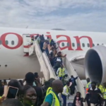 Crowd of passengers and ground crew in high-visibility vests boarding an Ethiopian Airlines plane via mobile stairs on the tarmac.