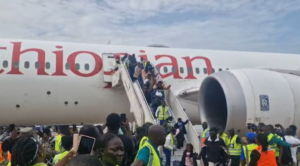 Crowd of passengers and ground crew in high-visibility vests boarding an Ethiopian Airlines plane via mobile stairs on the tarmac.