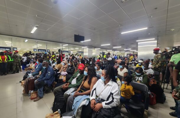 SA returnees | Ghanaguardian.com Crowd of travelers wearing masks seated in an airport waiting area with luggage, security personnel visible near counters in the background.