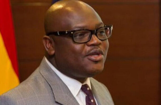 SIMON-MADJIE-1_1000x500-780x470 | Ghanaguardian.com Man in a gray suit and maroon tie, wearing glasses, speaking in a formal setting with a flag in the background.