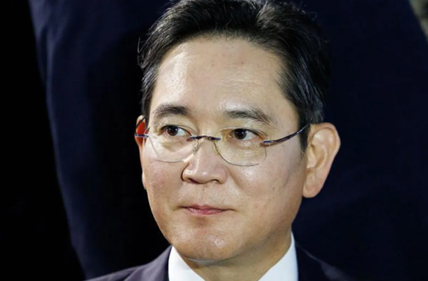 Man wearing glasses and a dark suit, looking to the side in a formal setting.