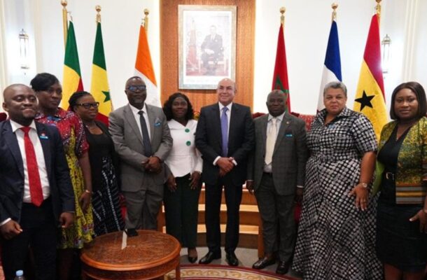 Screenshot 2026-05-12 070116 | Ghanaguardian.com Group of diverse professionals in suits and dresses posing in a formal meeting room with multiple national flags behind them