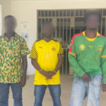 Five young men with blurred faces stand in a row outside a building, each wearing different casual or sports outfits including jerseys and patterned shirts.