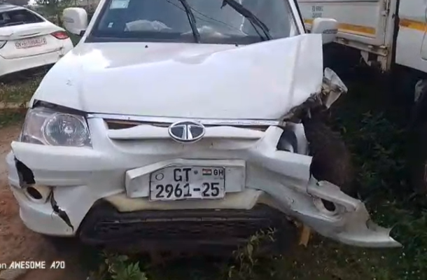 Screenshot-2026-05-16-115910 | Ghanaguardian.com White compact SUV with front-end collision damage, crumpled hood and bumper, license plate GT 2961-25 visible, parked beside a larger truck in a dirt lot.