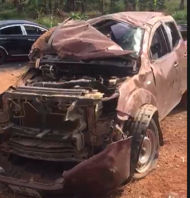 Brown SUV severely damaged at the front, with the hood crumpled and engine exposed, parked on a dirt lot.