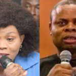 Two people speak into handheld microphones: a woman with a large curly hairstyle in a blue top on the left and a man in a black shirt on the right, both addressing an audience.
