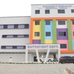 Front view of a hospital with a bright multicolored facade, 'Outpatient Dept' entrance, an ambulance and two cars in the driveway.
