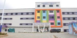Front view of a hospital with a bright multicolored facade, 'Outpatient Dept' entrance, an ambulance and two cars in the driveway.