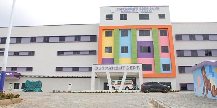 Front view of a hospital with a bright multicolored facade, 'Outpatient Dept' entrance, an ambulance and two cars in the driveway.