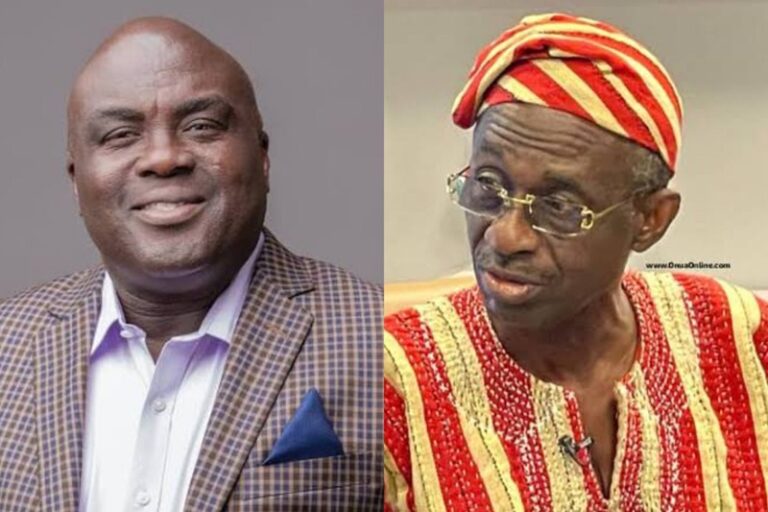 Two men side by side: one in a checkered blazer and light shirt smiling, the other in red-gold traditional clothing with a headwrap and glasses looking to the side.