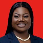Professional headshot of a smiling Black woman in a navy blazer and pearl necklace against a solid red background.