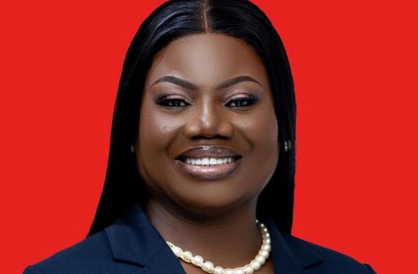 Professional headshot of a smiling Black woman in a navy blazer and pearl necklace against a solid red background.