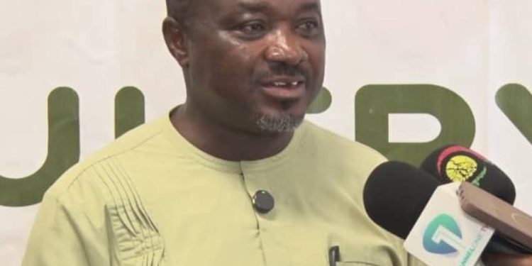 Man in a light green traditional outfit speaks into a microphone during an interview.