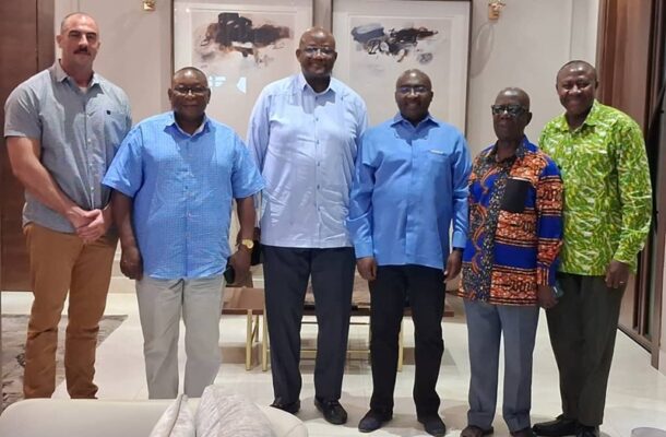 Six men stand side by side indoors, posing for a group photo in a hallway or reception area.