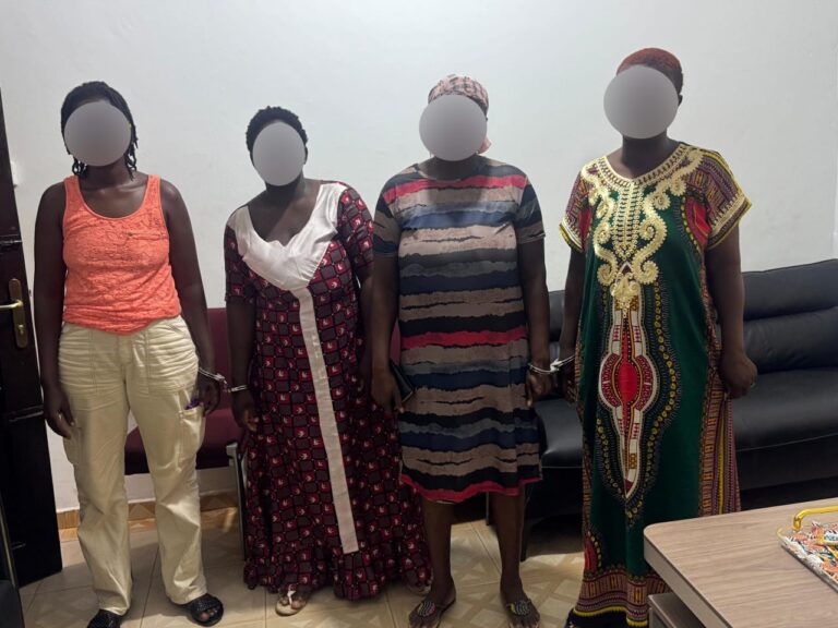 Four women with blurred faces pose indoors against a light wall, each wearing a distinct colorful dress.