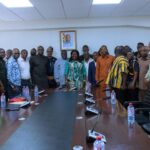Group of professionals standing in a boardroom around a long conference table for a formal meeting in session.