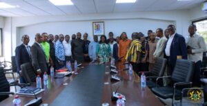 Group of professionals standing in a boardroom around a long conference table for a formal meeting in session.