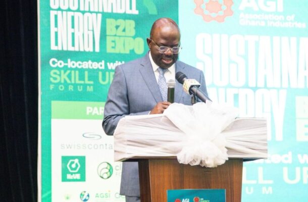 Man in a blue suit speaks at a podium with microphone during a conference; bold teal backdrop says 'Sustainable' and 'Energy Expo' behind him.